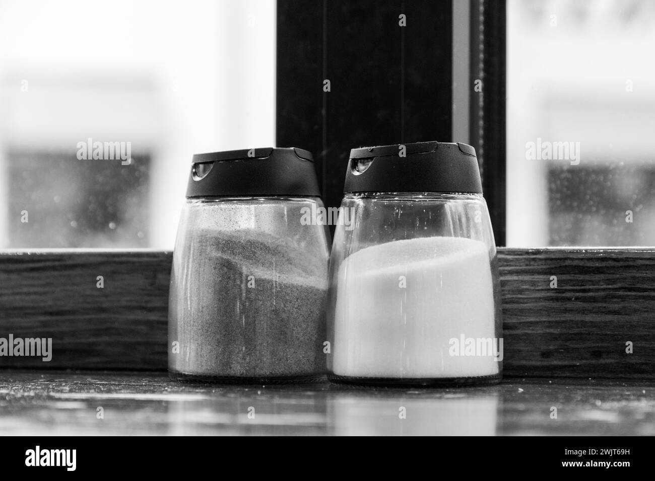 Salière et poivrière sur une table contre une fenêtre dans un diner. Image monochrome Banque D'Images