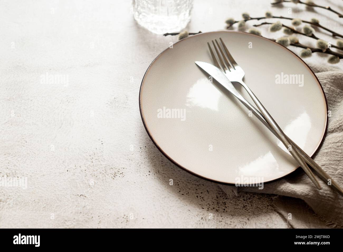 Table de Pâques avec assiette en céramique blanche vide avec couverts et branches de saule printanier sur table blanche. Couleurs neutres. Fond de Pâques. Banque D'Images