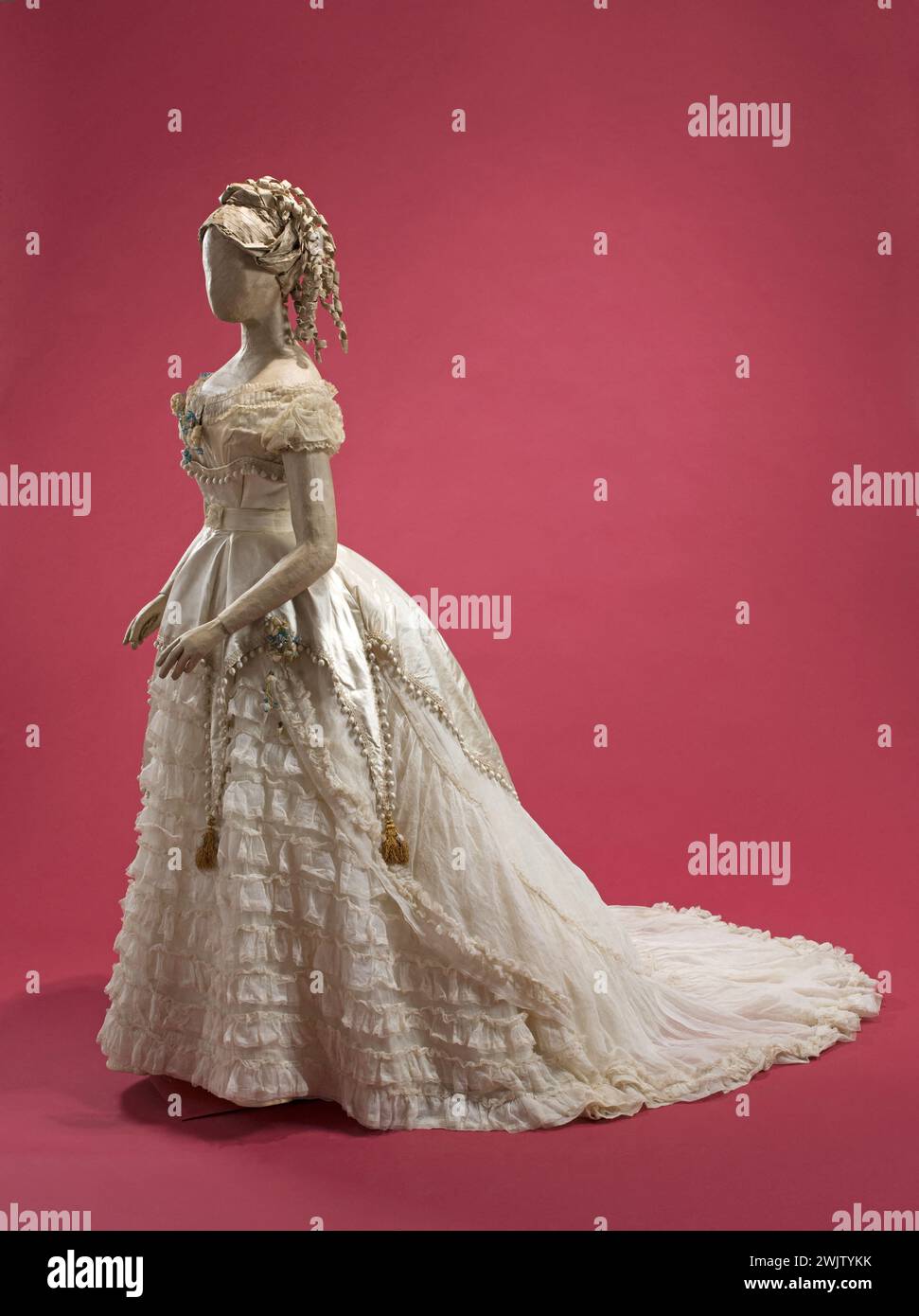 Blouse de balle. Peplum -robe formant un train. Corsage court en mousseline de coton. Décolleté avec plissé et bouquet de roses blanches et myosotis. Jupe mousseline recouverte de neuf volants. Mousseline sur-jupe formant pouf, bordé par un grand volant. Péplum en satin blanc formant corselet garni de pompons de soie tombant en quatre côtés terminés par des glands en soie et perles, polis derrière. Tresse de verre sur le bord. 1866. Galliera, musée de la mode de la ville de Paris. Forme, mousseline de coton, peplum, blouse de balle, satin, second empire Banque D'Images