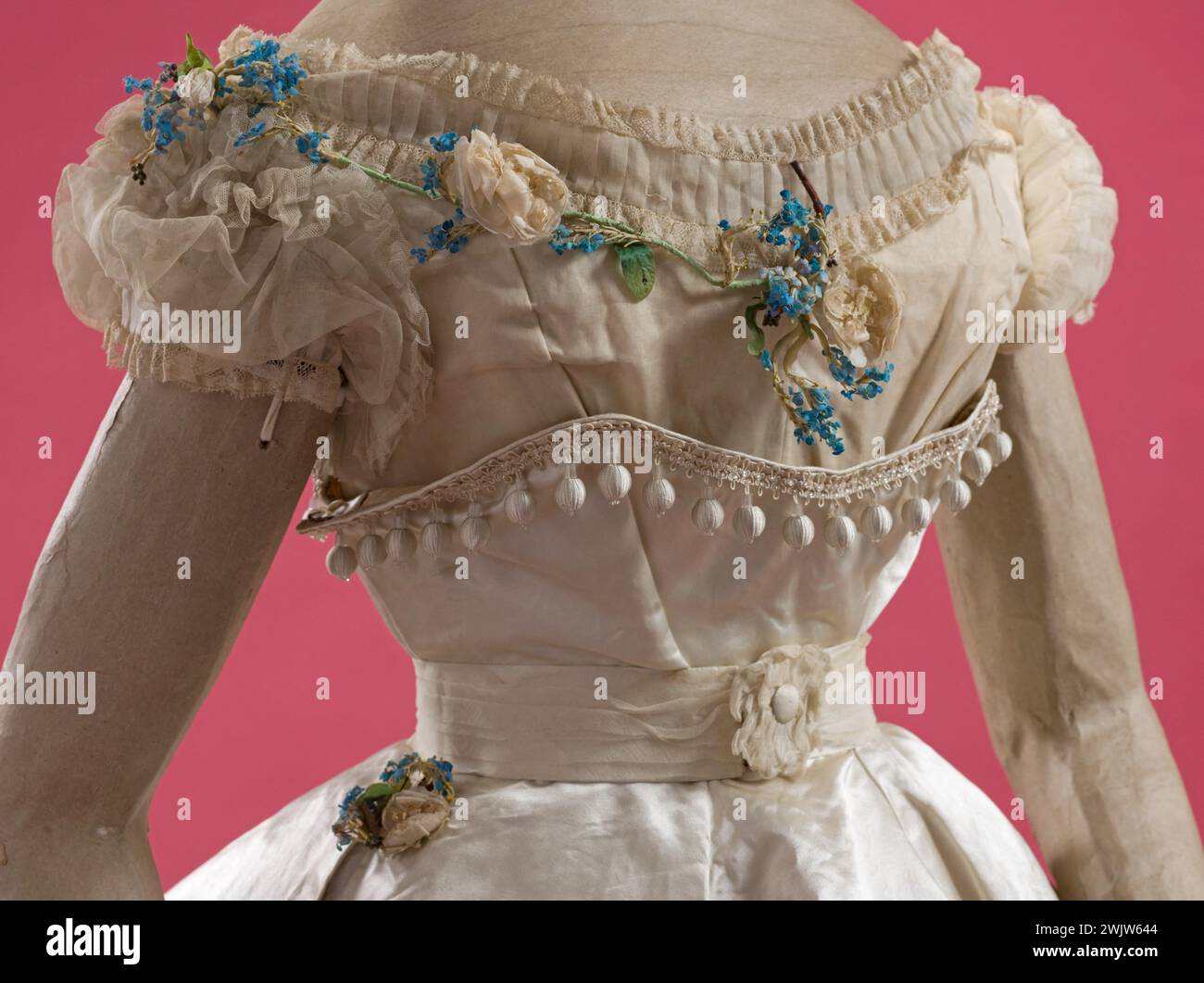 Robe de bal (détail). Peplum -robe formant un train. Corsage court en mousseline de coton. Décolleté avec plissé et bouquet de roses blanches et myosotis. Jupe mousseline recouverte de neuf volants. Mousseline sur-jupe formant pouf, bordé par un grand volant. Péplum en satin blanc formant corselet garni de pompons de soie tombant en quatre côtés terminés par des glands en soie et perles, polis derrière. Tresse de verre sur le bord. 1866-1867. Galliera, musée de la mode de la ville de Paris. Robe de balle (détail) dos, féminin, mousseline de coton, peplum, pompon de soie, blouse de balle, satin, seco Banque D'Images