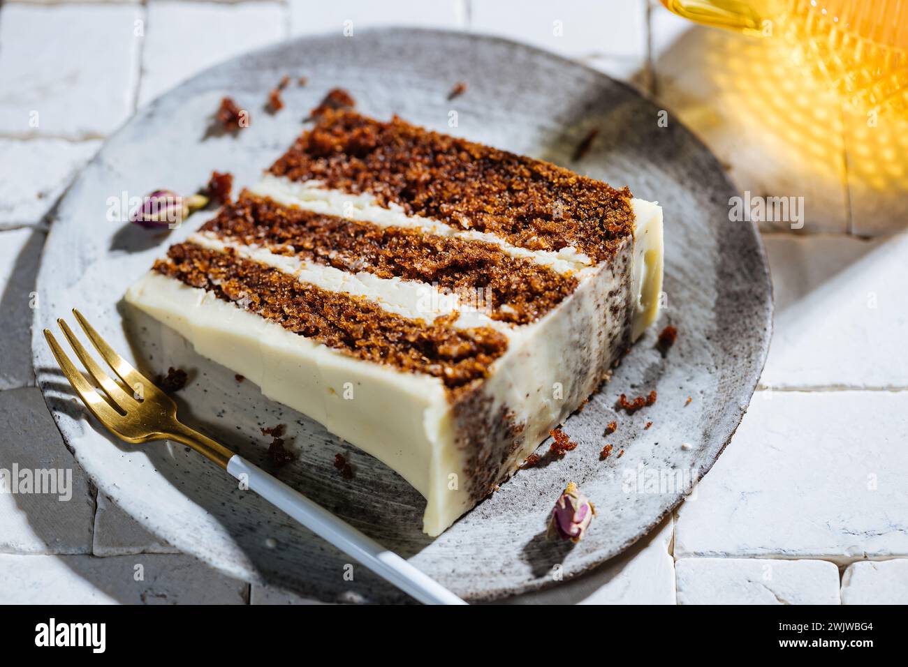 Un morceau de gâteau aux carottes servi sur une table en carreaux blancs. scène ensoleillée lumineuse. Gâteau en couches avec glaçage au fromage à la crème et biscuit moelleux avec boisson Banque D'Images