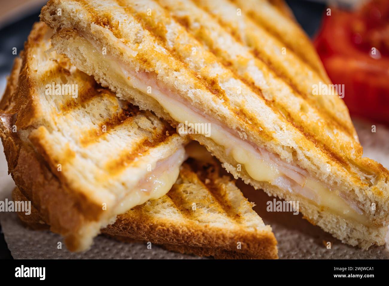 Sandwich toast coupé en tranches avec fromage Gouda fondu et jambon de dinde sur fond de bois avec tomate cerise sur une assiette noire. Servi avec du thé glacé. Banque D'Images