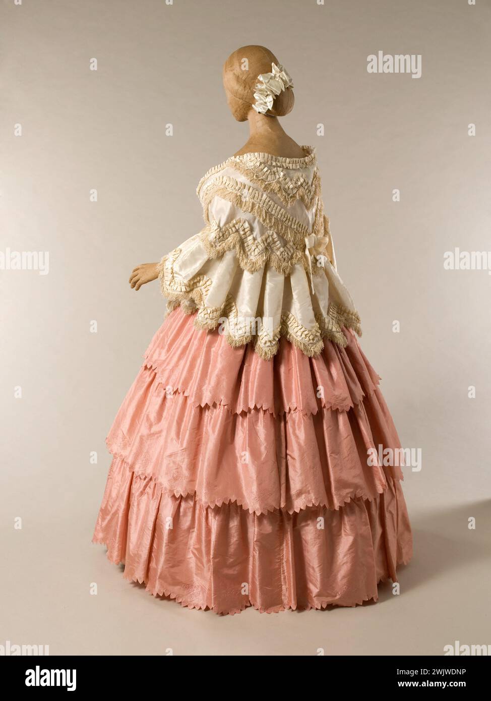 Manteau de mariage et robe de bal. Mantelet : taffetas ivoire, franges bouclées et chenille, orné d'une ruche. Robe : taffetas barrés rose et crème, gaufré sur les feuilles de rose, volant, ruban de taffetas rose. Vers 1853-1856. Galliera, musée de la mode de la ville de Paris. Robe de mariage et de balle féminine, frange, mannequin, manteau de mariage, robe de balle, ruban, rose, second empire, soie, taffetas ivoire, volant, crinoline Banque D'Images