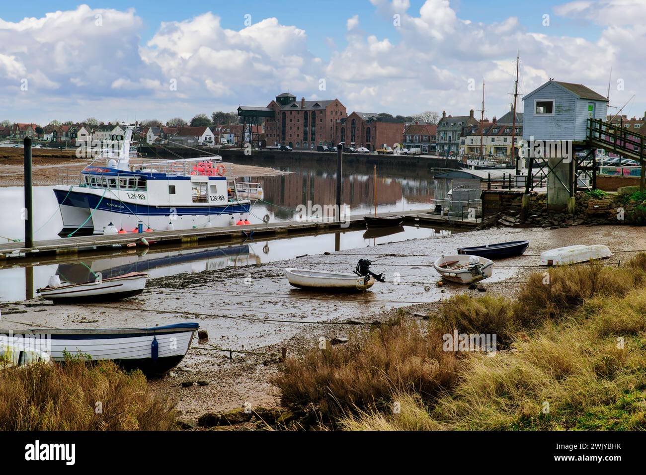 Wells-next-the-Sea, Norfolk, Angleterre, Royaume-Uni - bateaux amarrés à la jetée et sur la plage dans le port à marée haute. La cabane bleue est la station d'enregistrement des marées Banque D'Images