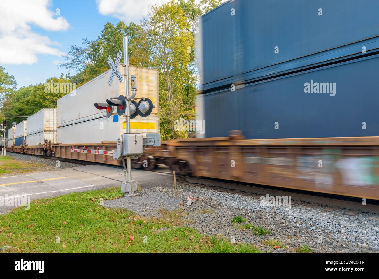 Train de conteneurs en mouvement rapide passant un passage à niveau par un matin ensoleillé d'automne Banque D'Images