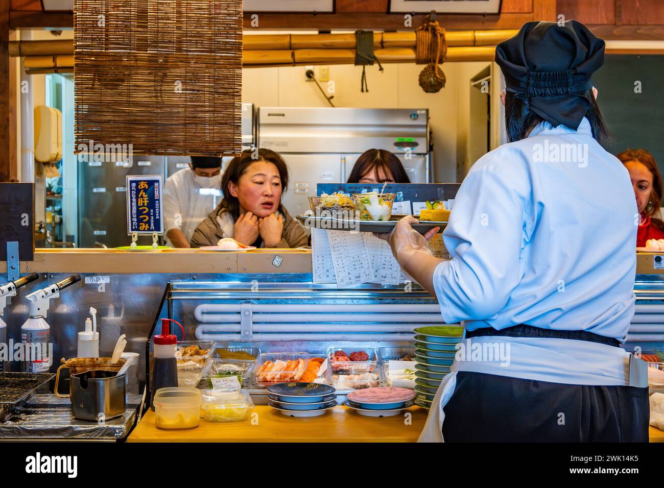 Chef cuisinant derrière le comptoir dans un restaurant Kaiten-sushi qui sert de petites assiettes de nourriture sur un tapis roulant. Hokkaido, Japon. Banque D'Images