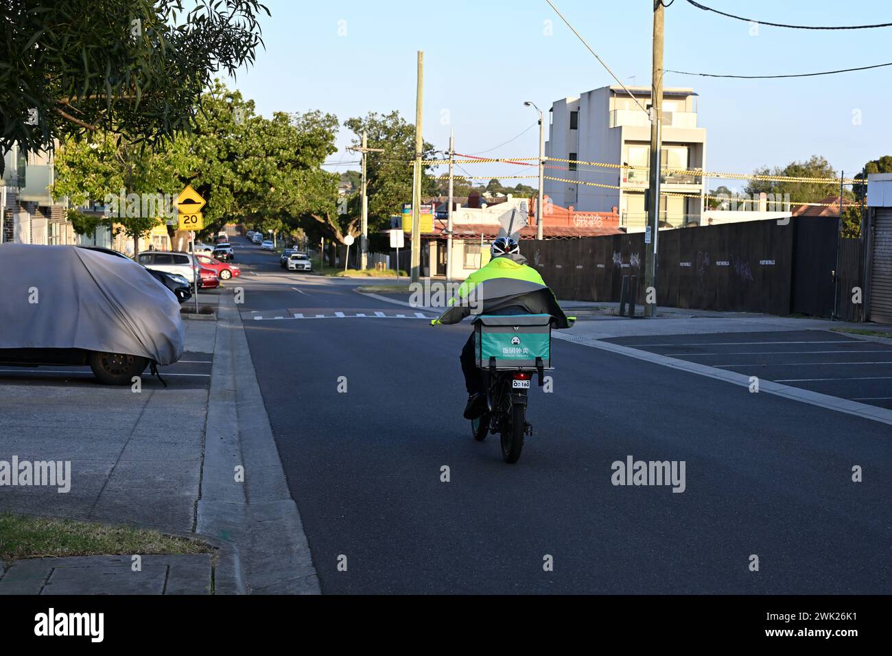 Vue arrière d'un livreur Fantuan, sur un vélo, alors qu'ils descendent une rue calme et ombragée de la banlieue de Melbourne Banque D'Images