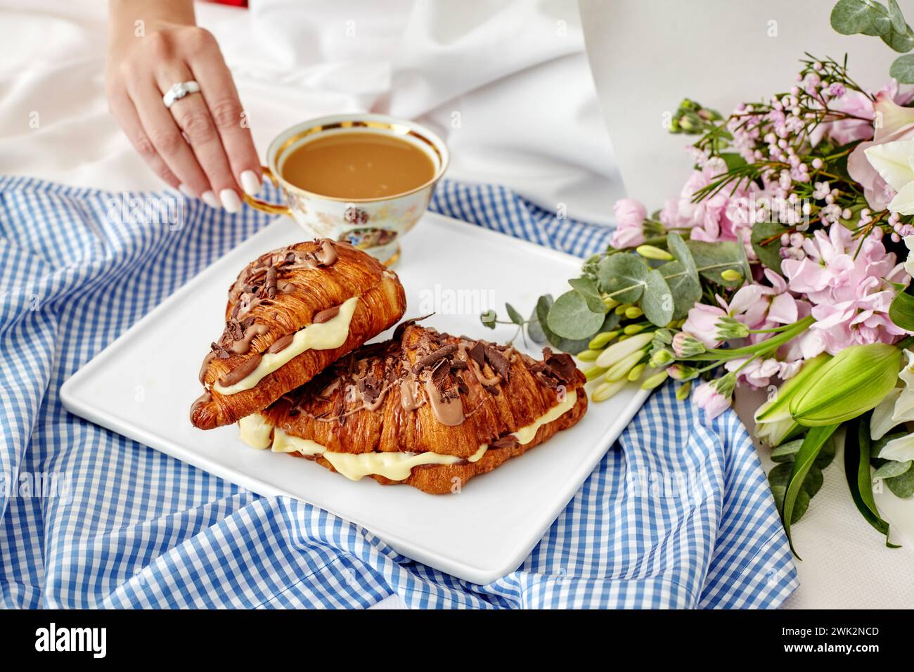 Romantique petit déjeuner intime dans la scène de lit avec femme atteignant pour une tasse de café, croissants français frais avec crème anglaise délicate et chocolat, et luxuriant Banque D'Images