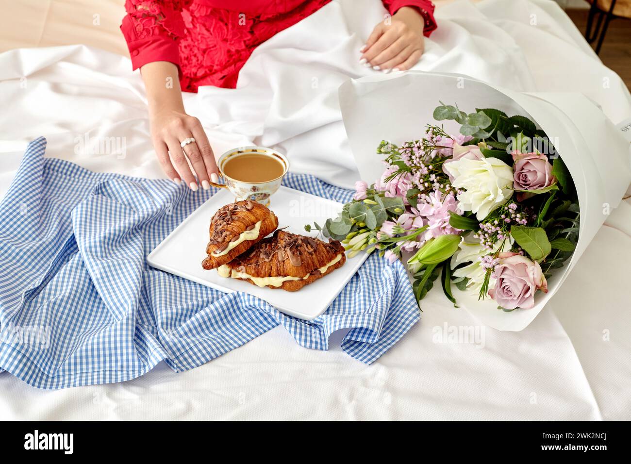 Élégant cadre romantique du matin avec femme en rouge appréciant le petit déjeuner au lit avec des croissants au chocolat français frais remplis de crème anglaise délicate et t Banque D'Images