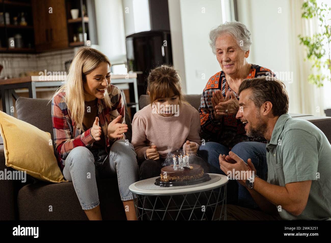 Une scène réconfortante se déroule alors qu'une famille multigénérationnelle se réunit sur un canapé pour présenter un gâteau d'anniversaire à une grand-mère ravie, créant ainsi des souvenirs Banque D'Images