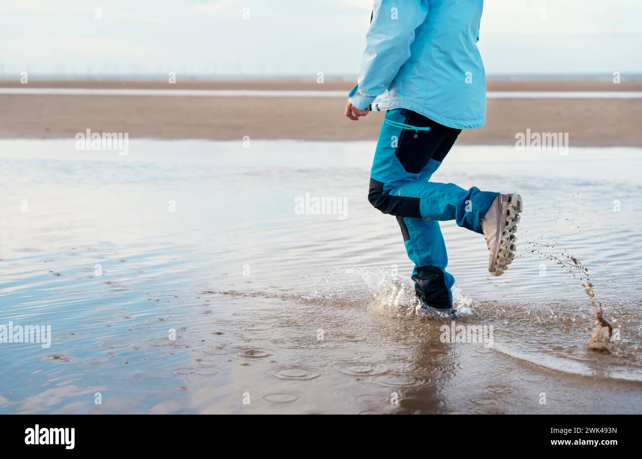 femme en pantalon waterproove bleu et bottes courir sur la plage. Concept de style de vie de voyage Banque D'Images
