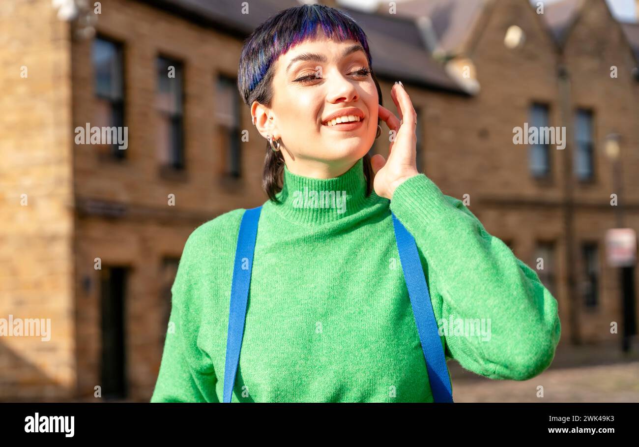 Une joyeuse jeune femme en vacances. Un touriste avec un sac à dos, vêtu d'un pull vert se promène dans une vieille ville européenne en vacances. Banque D'Images
