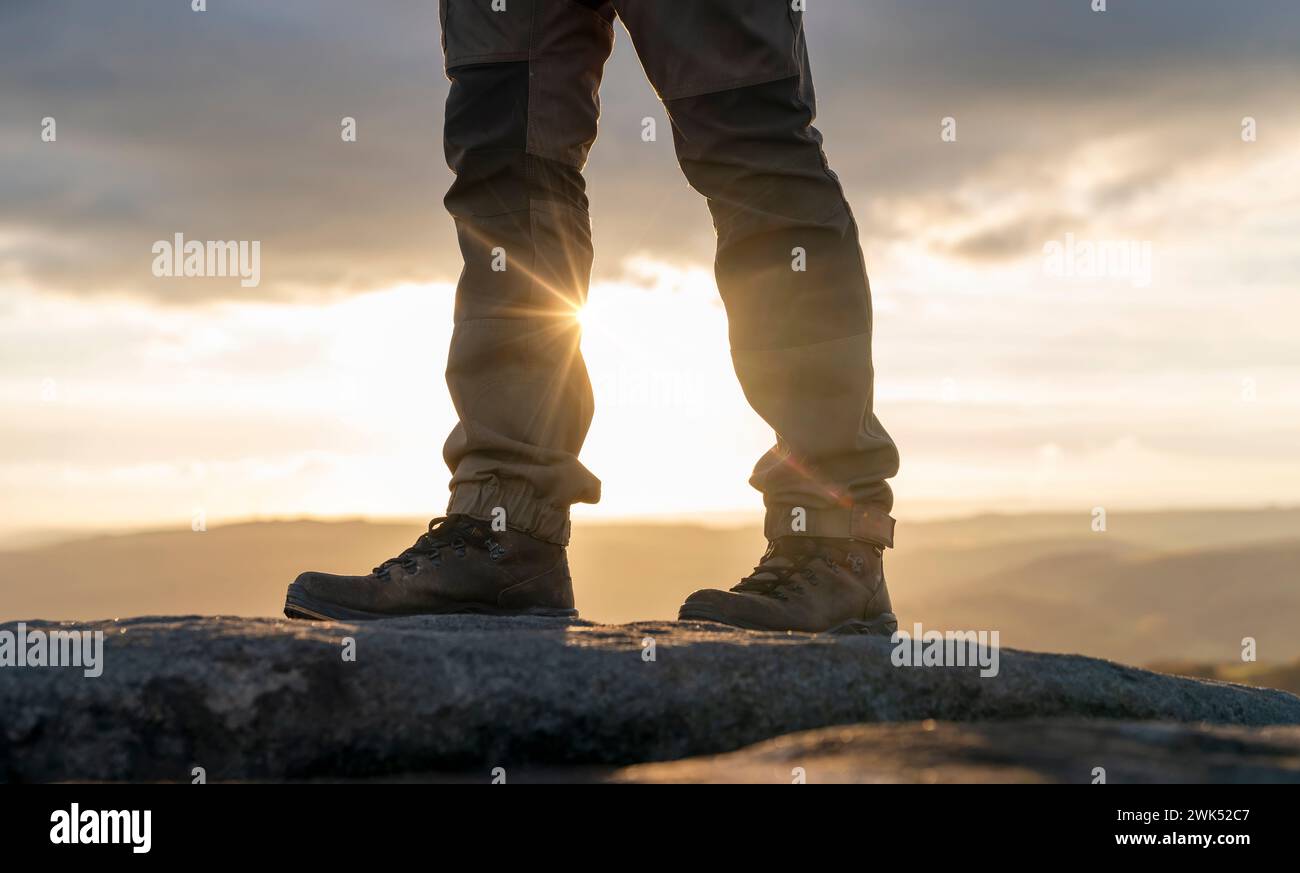 Homme dans des bottes spéciales marchant dans les montagnes atteignant la destination et sur le sommet de la montagne dans Peak District au coucher du soleil le jour d'automne voyage vie Banque D'Images