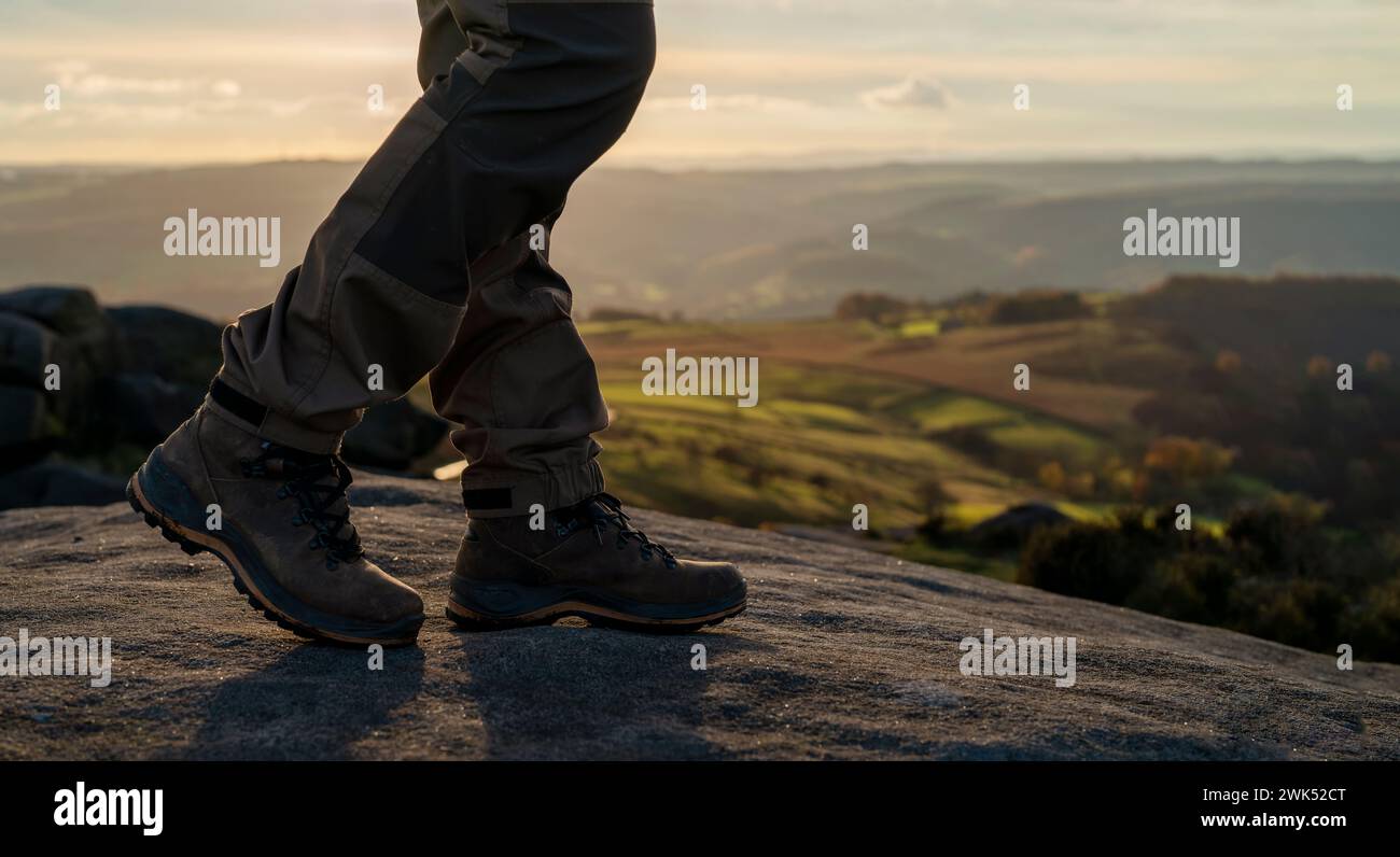 Homme dans des bottes spéciales marchant dans les montagnes atteignant la destination et sur le sommet de la montagne dans Peak District au coucher du soleil le jour d'automne voyage vie Banque D'Images