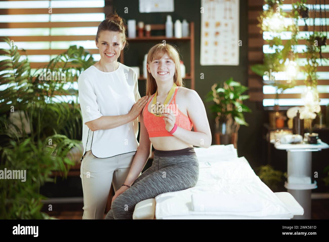 Temps de soins. massothérapeute médicale féminine heureuse dans l'armoire de massage avec client adolescent et médaille d'or. Banque D'Images