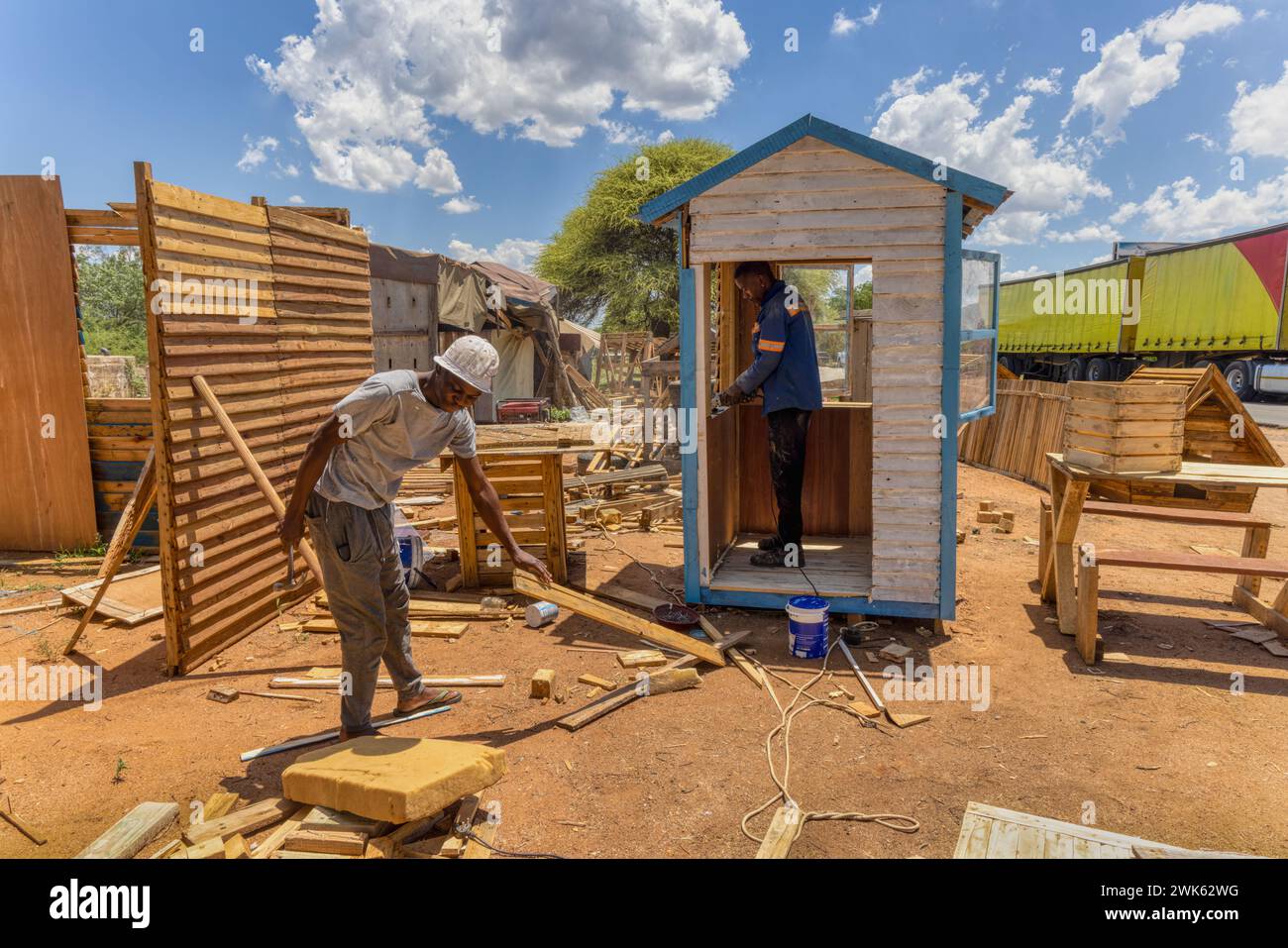 deux ouvriers afro-américains fabriquant une maison wendy, hangar en bois à l'extérieur, l'un utilise une meuleuse d'angle pour lisser la fenêtre, l'autre marteau un Banque D'Images