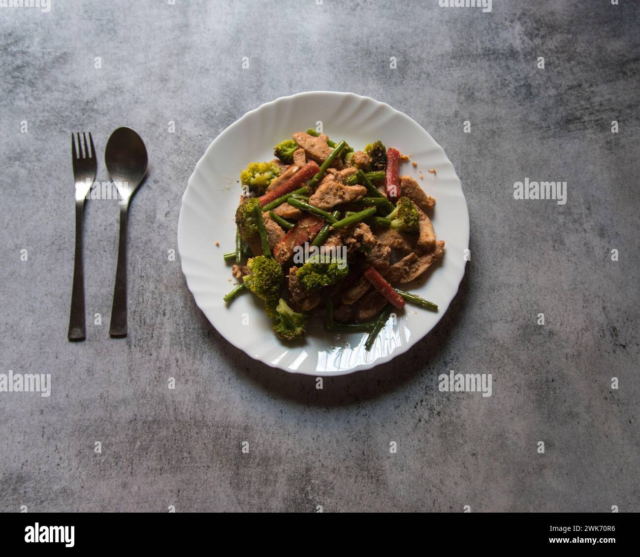 Vue du dessus du poulet frit à la poêle et des légumes servis dans une assiette blanche. Banque D'Images
