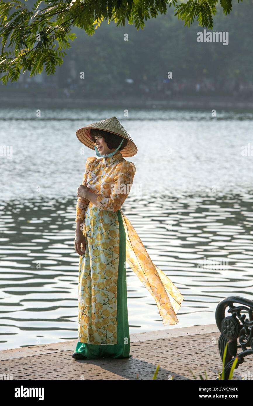 Femme en robe traditionnelle et chapeau conique au lac Hoan Kiem à Hanoi, Vietnam Banque D'Images