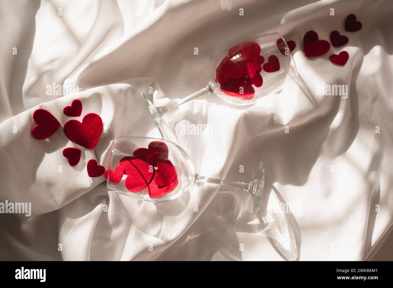 Verres à vin avec des coeurs rouges sur feuille blanche à la lumière du soleil Banque D'Images