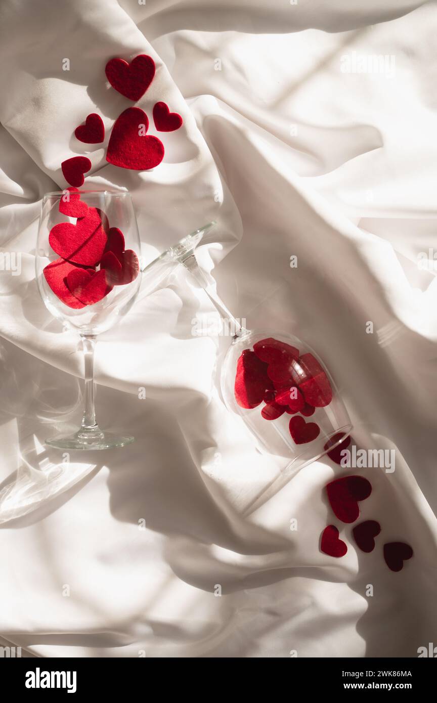 Deux verres à vin avec des coeurs en tissu sur drap de lit blanc au soleil Banque D'Images