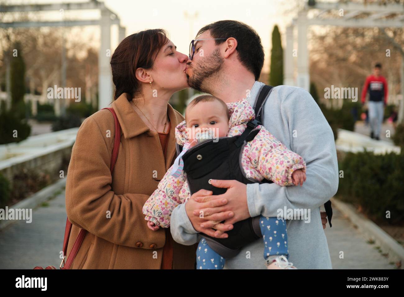 Couple embrassant et tenant leur bébé de 6 mois dans un porte-bébé. Banque D'Images