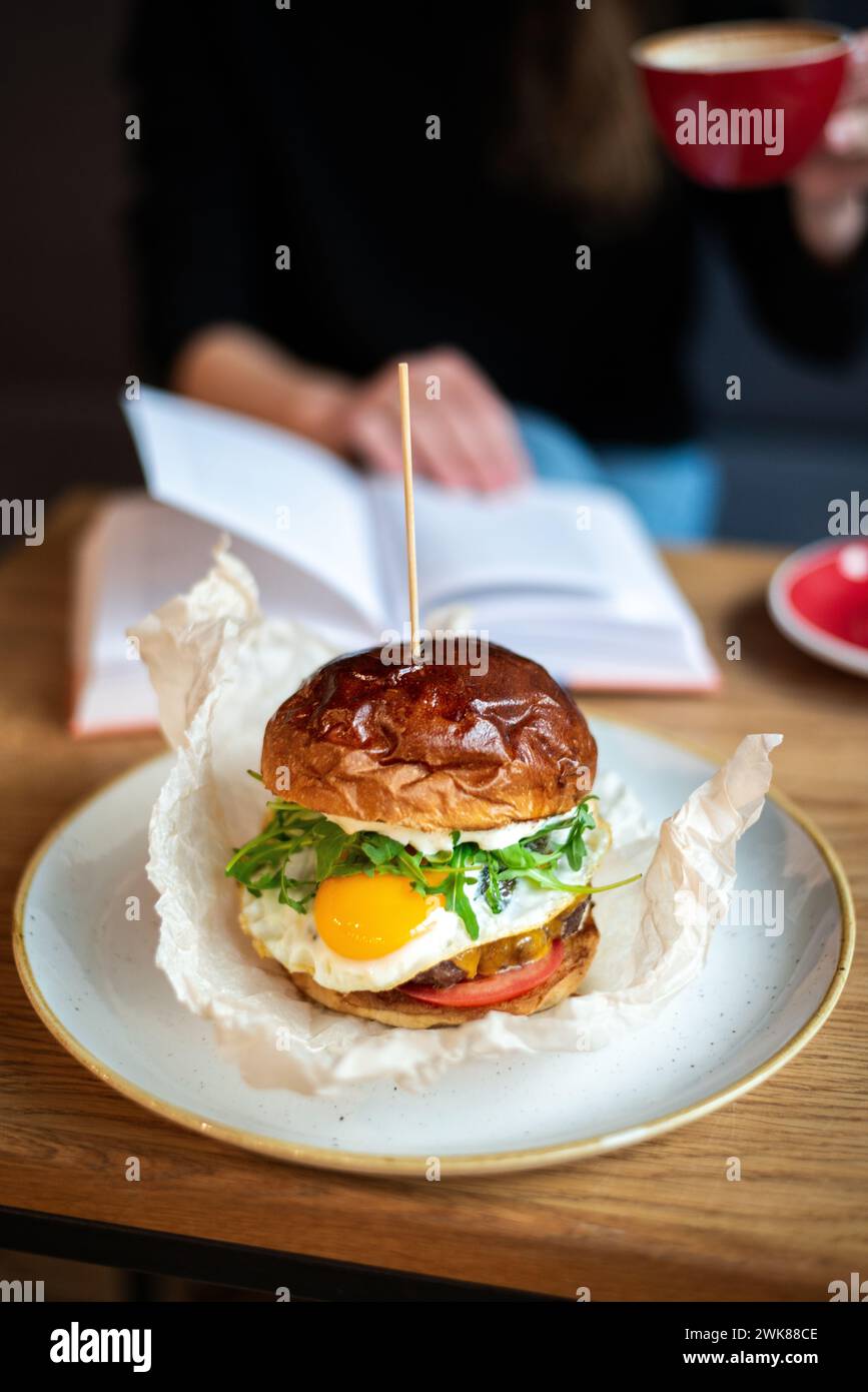 Gros plan Burger avec œuf frit avec femme en arrière-plan Banque D'Images