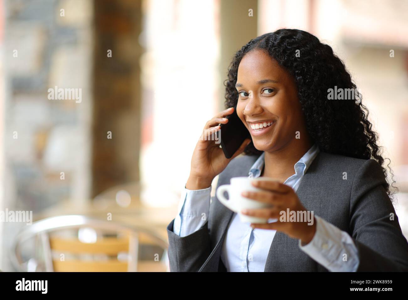 Heureux cadre noir boire et parler au téléphone en vous regardant dans une terrasse de café Banque D'Images