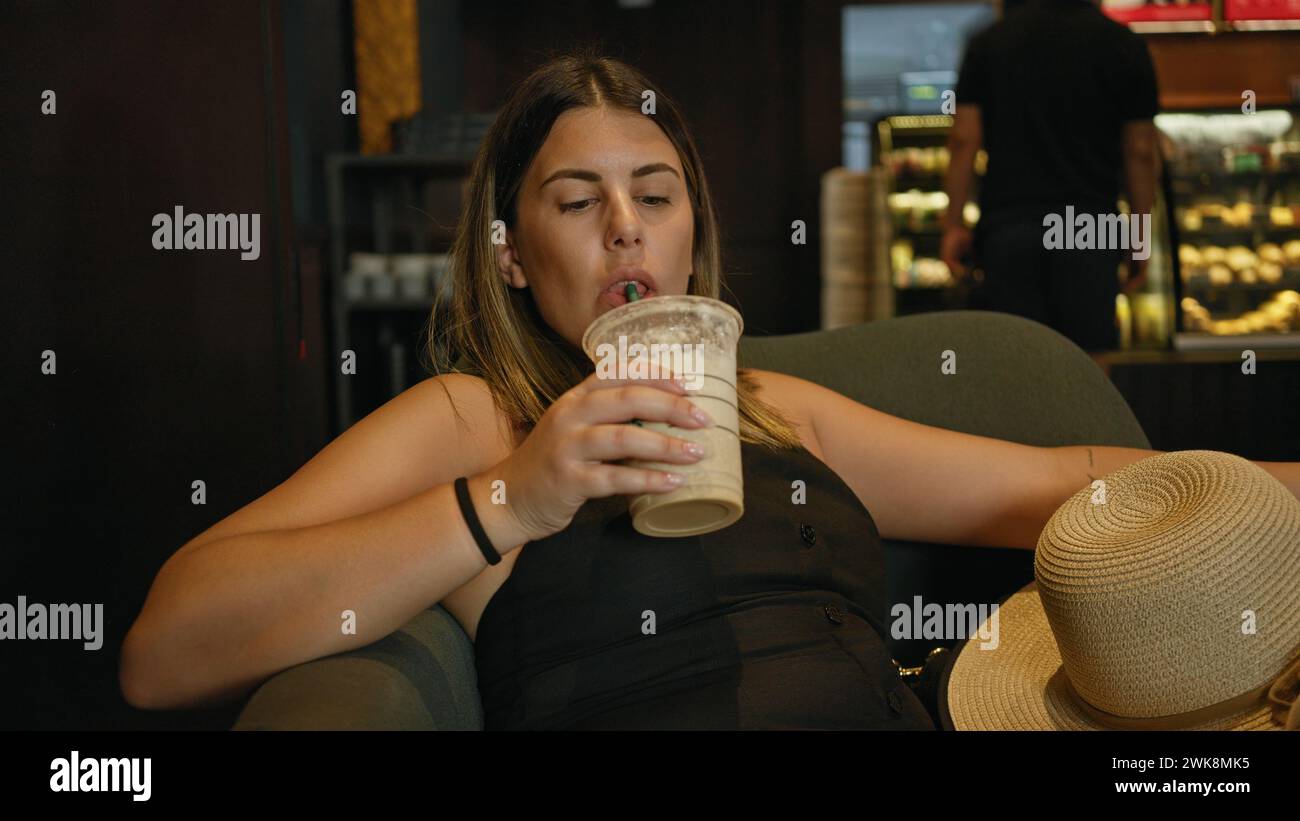 Une jeune femme détendue sirote une frappe dans un environnement de café confortable, exsudant des loisirs décontractés. Banque D'Images