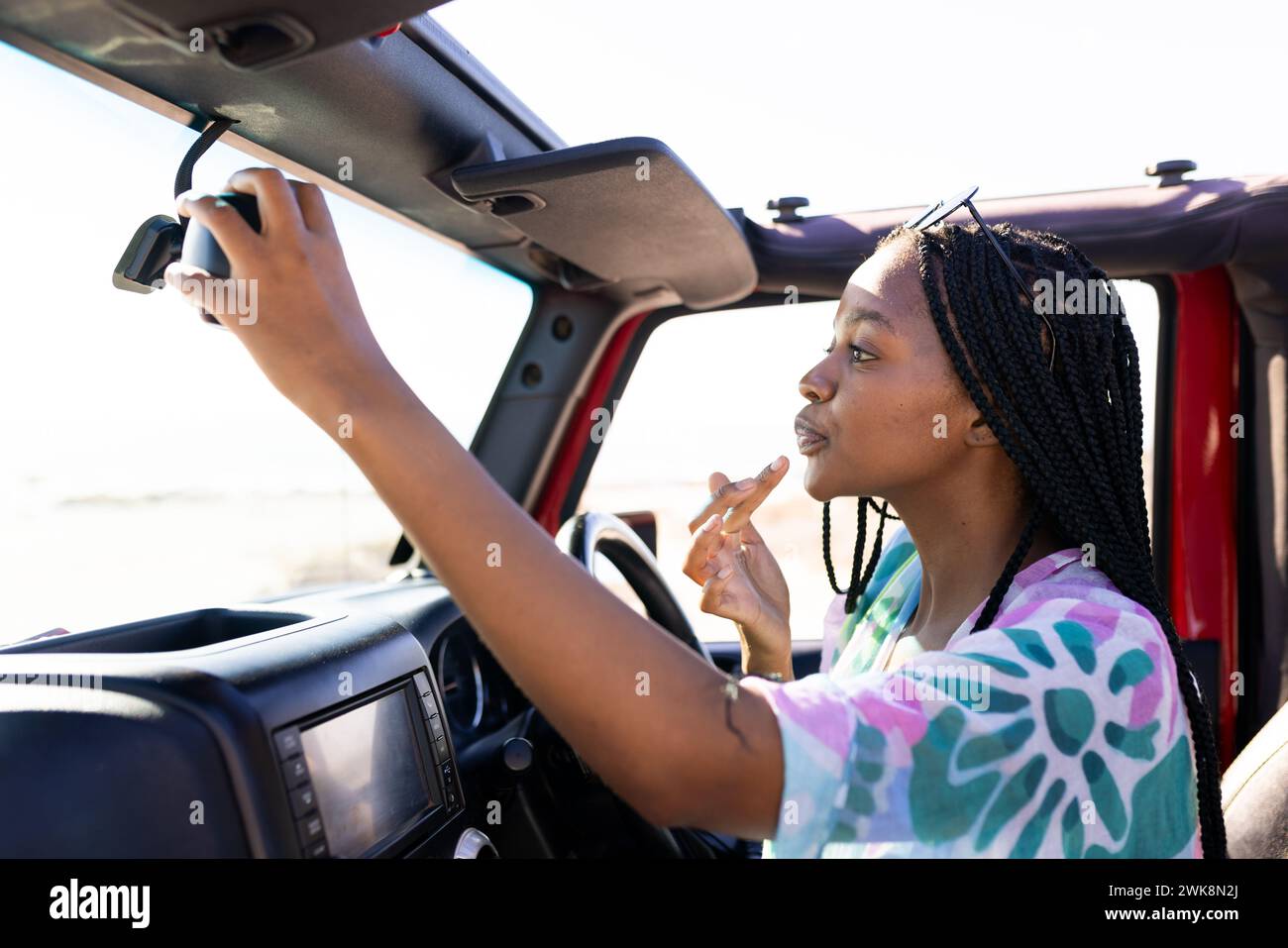 Jeune femme afro-américaine ajuste le rétroviseur dans une voiture lors d'un voyage sur la route Banque D'Images