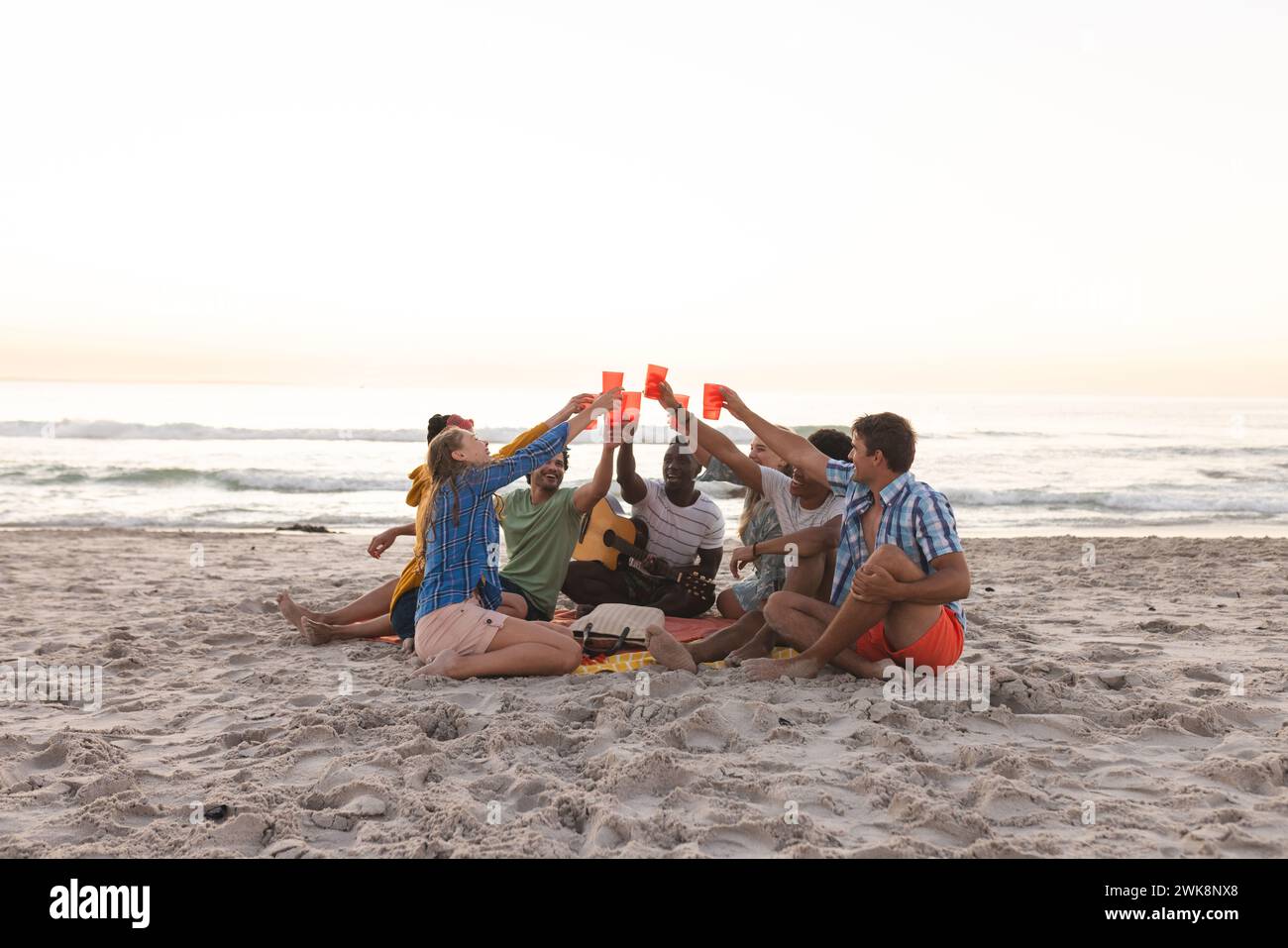 Groupe diversifié d'amis toast sur une plage au coucher du soleil, ayant une fête Banque D'Images