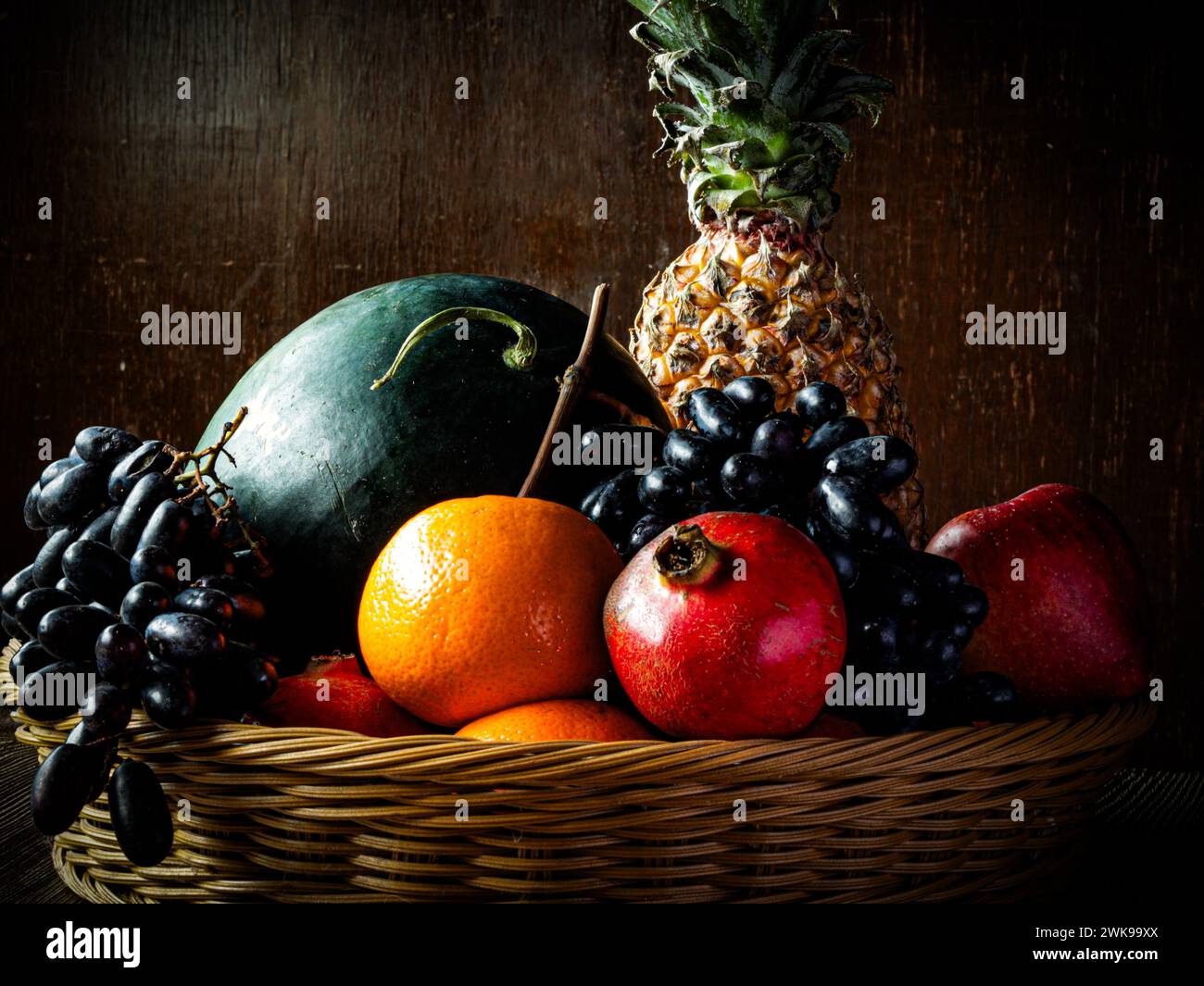 Les fruits assortis dans un panier sur une vieille table en bois sur fond marron noyer. Banque D'Images