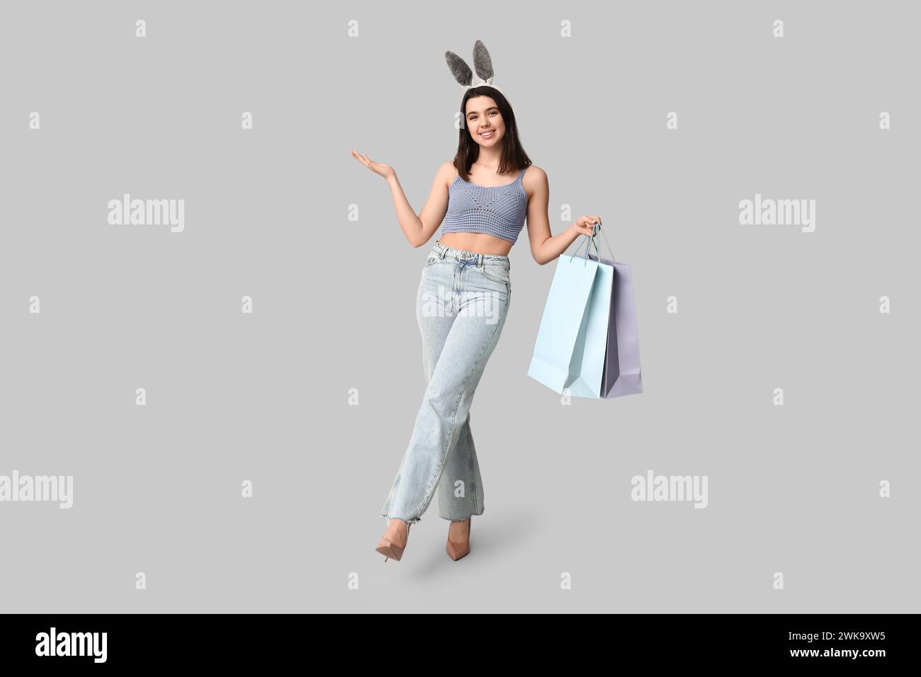Belle jeune femme heureuse dans des oreilles de lapin avec des sacs à provisions sur fond gris. Fête de Pâques Banque D'Images