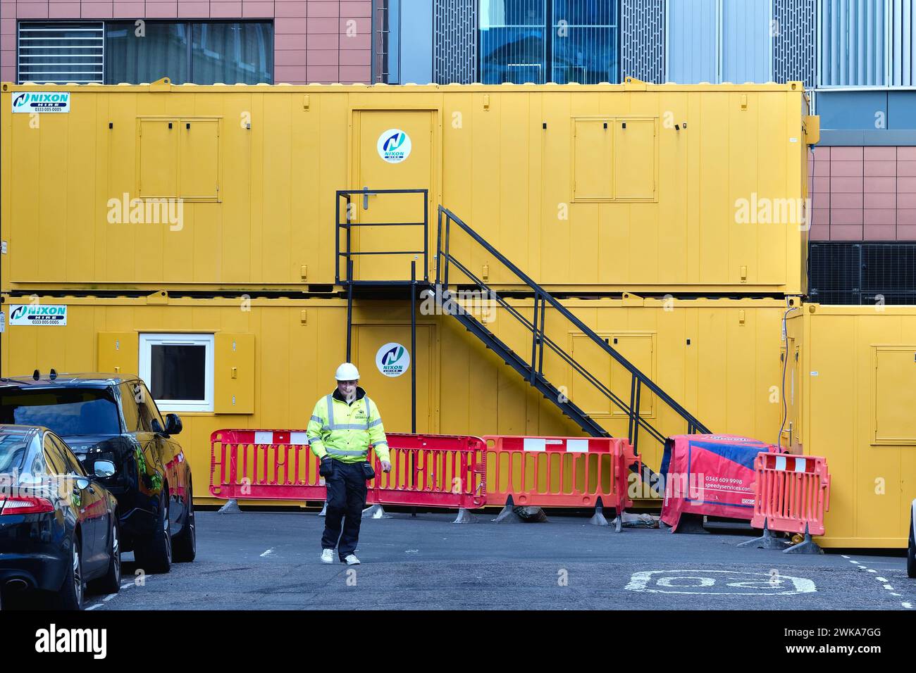 Cabines temporaires de grands constructeurs jaunes créant des formes abstraites avec travailleur en veste haute viz et casque de sécurité à Leyden Street Aldgate Londres Angleterre Banque D'Images