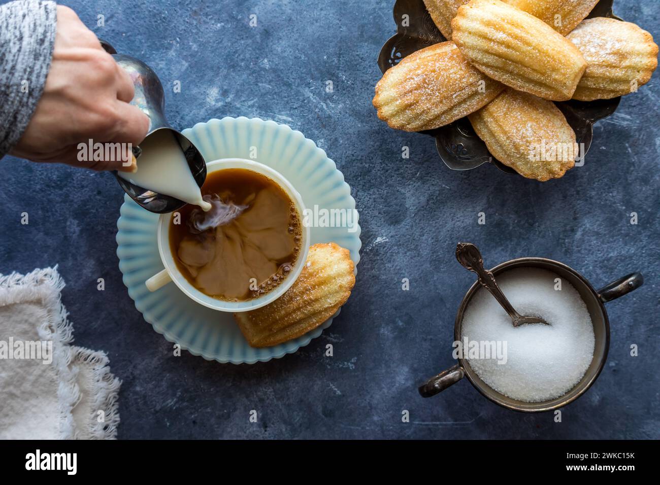 Crème versée dans une tasse de café servie avec des Madeleines françaises. Banque D'Images