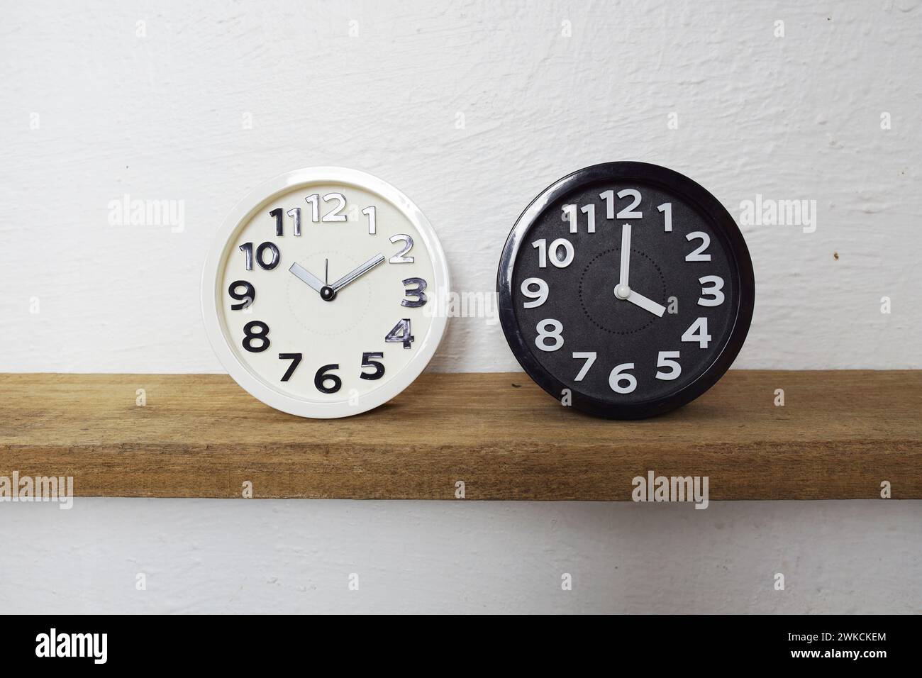 L'horloge Alram blanche et noire montre la différence de temps sur les étagères en bois Banque D'Images