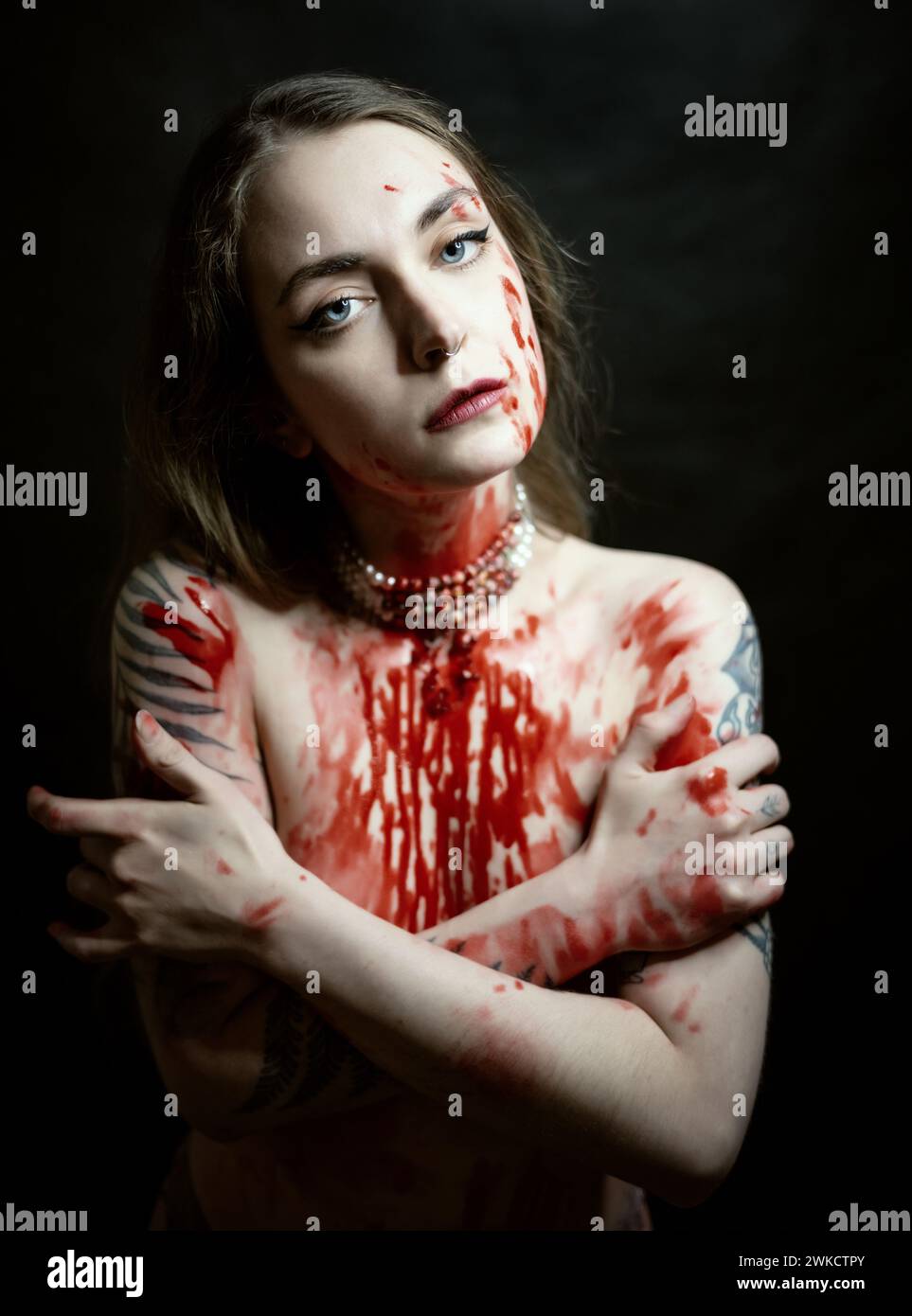 Portrait de jeune femme avec de la peinture rouge sur sa poitrine sur fond sombre. Banque D'Images