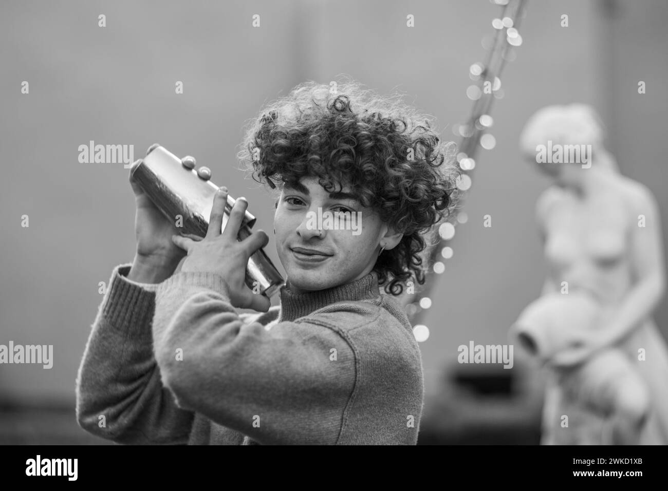 caucasien jeune barista aux cheveux rouges frais mélangeant cocktail dans shaker avec énergie à l'extérieur dans un événement privé en hiver Banque D'Images