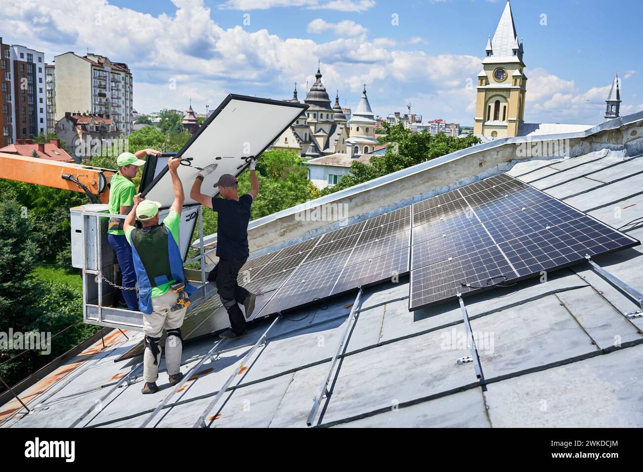 Ouvriers construisant un système de panneau solaire sur le toit en métal avec l'aide d'un ascenseur de grue en milieu urbain. Hommes installateurs transportant le module solaire photovoltaïque à l'extérieur. Concept de génération d'énergie renouvelable. Banque D'Images