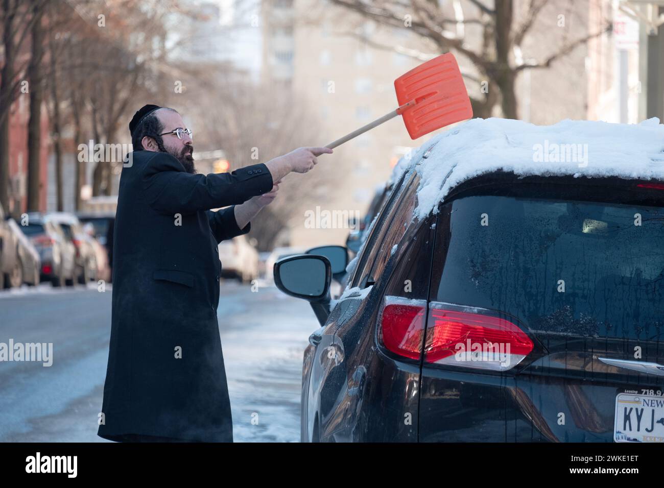 Par un froid matin d'hiver, un homme juif orthodoxe nettoie la neige de son SUV Banque D'Images