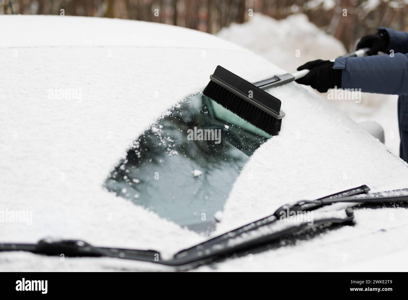 homme enlevant la neige de son pare-brise de voiture avec une grosse brosse Banque D'Images