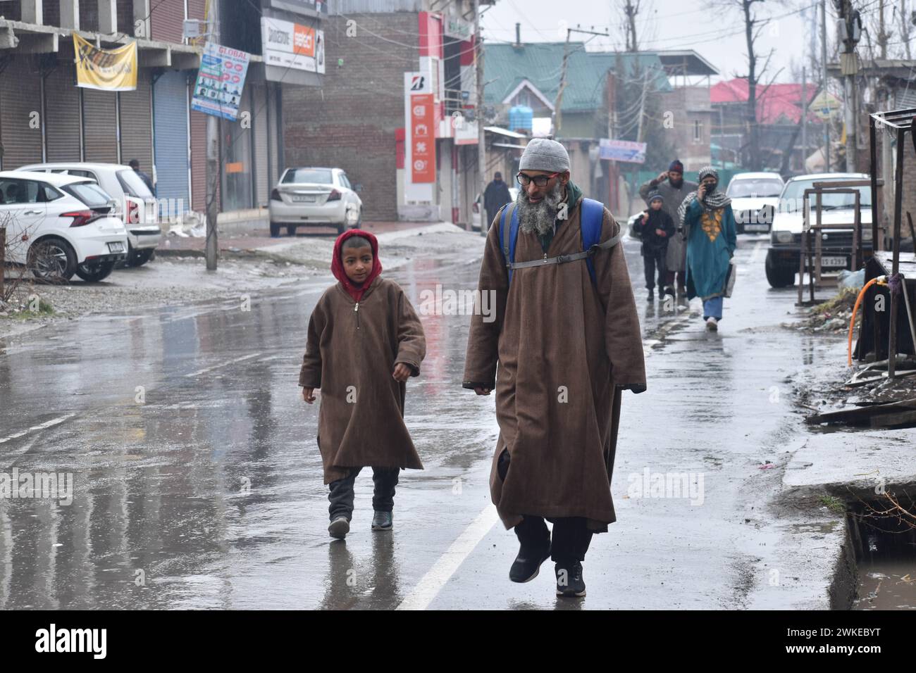 Srinagar, Inde. 18 février 2024. À Srinagar, au Cachemire, en Inde, le 18 février 2024 : un père et son fils se promènent sur les routes baignées de pluie, vêtus de phérans traditionnels, alors que la région célèbre des précipitations opportunes et rafraîchissantes. Dans le contexte de hautes étendues enneigées, une prévision météorologique promet un paradis hivernal fantaisiste, avec de fortes chutes de neige attendues du 18 au 20 février. (Photo de Danish Showkat/Sipa USA) crédit : Sipa USA/Alamy Live News Banque D'Images