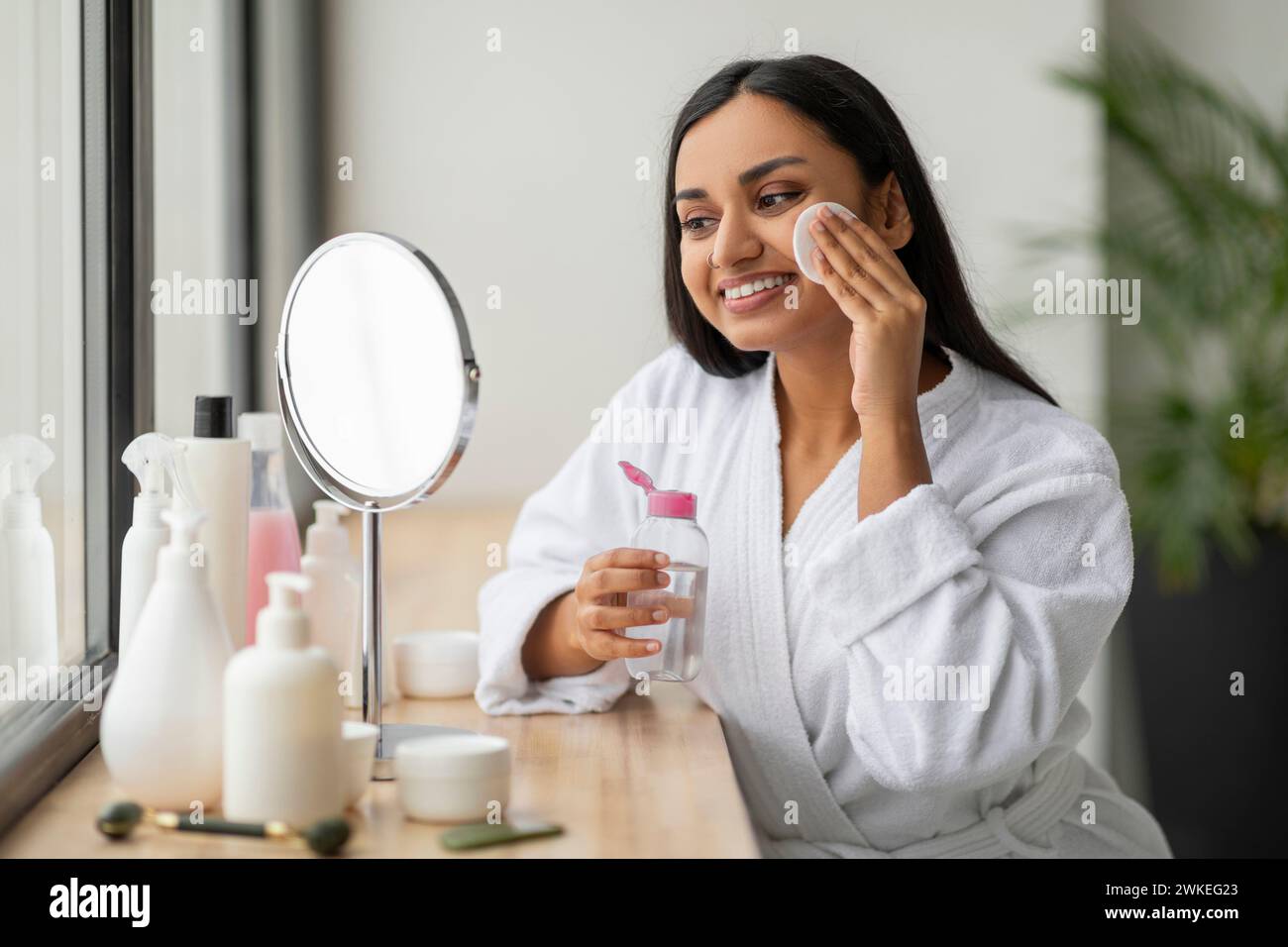 Positive jeune femme indienne nettoyant le visage dans la salle de bain Banque D'Images
