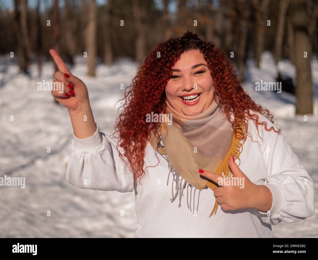 Une femme aux cheveux rouges dans un sweat-shirt blanc. Une fille qui se berce dans le parc en hiver. Banque D'Images