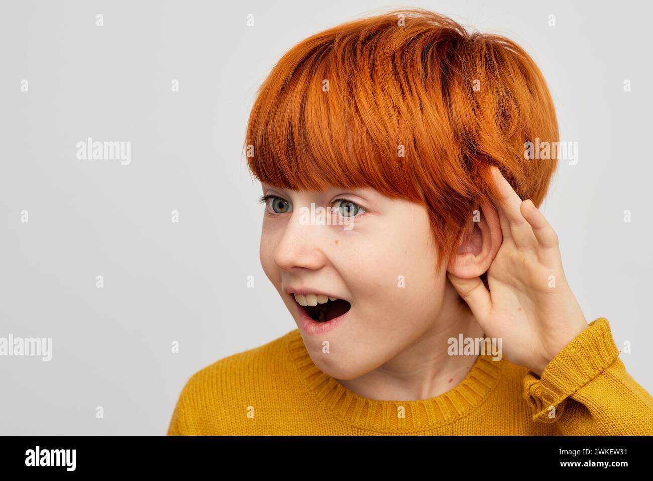 Beau garçon aux cheveux roux écoutant le son de la main près de l'oreille pour le contrôle auditif Banque D'Images