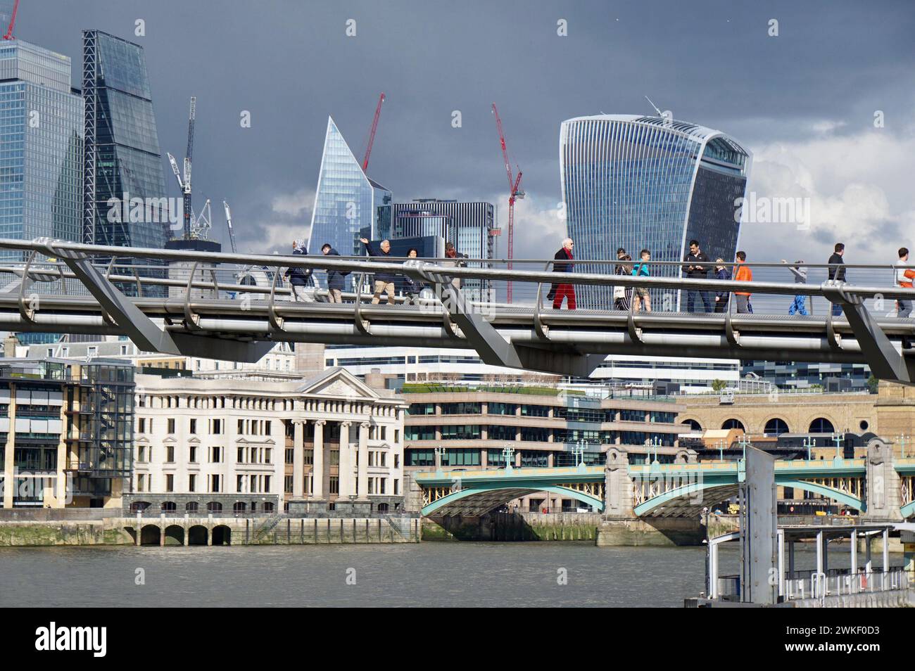 Millennium Bridge traversant les gratte-ciel modernes de Londres par une journée ensoleillée avec un fond spectaculaire de ciel orageux. Banque D'Images