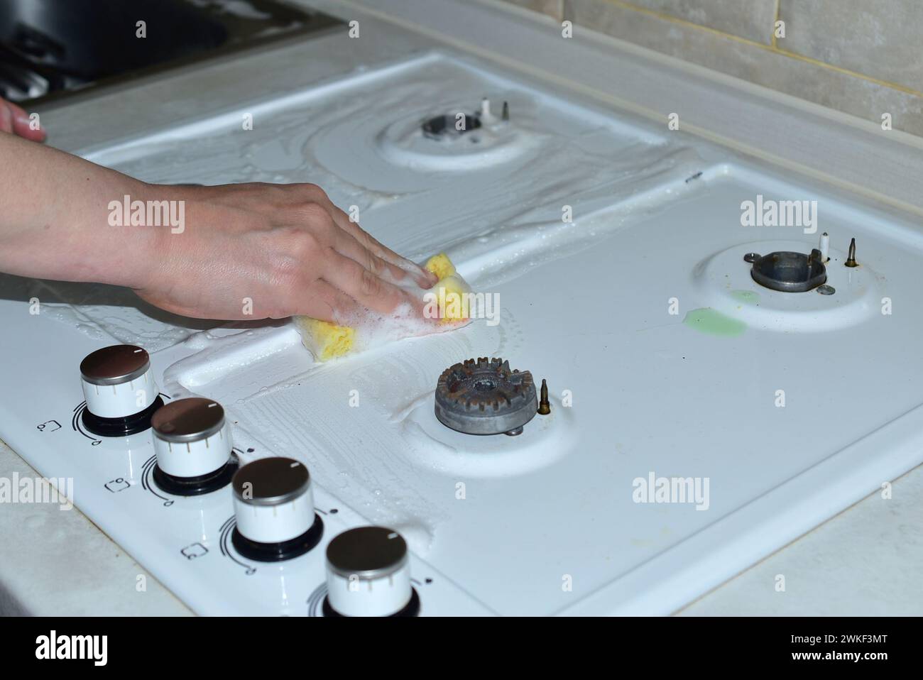Une femme lave la surface supérieure d'une cuisinière à gaz avec une éponge et des détergents. Banque D'Images