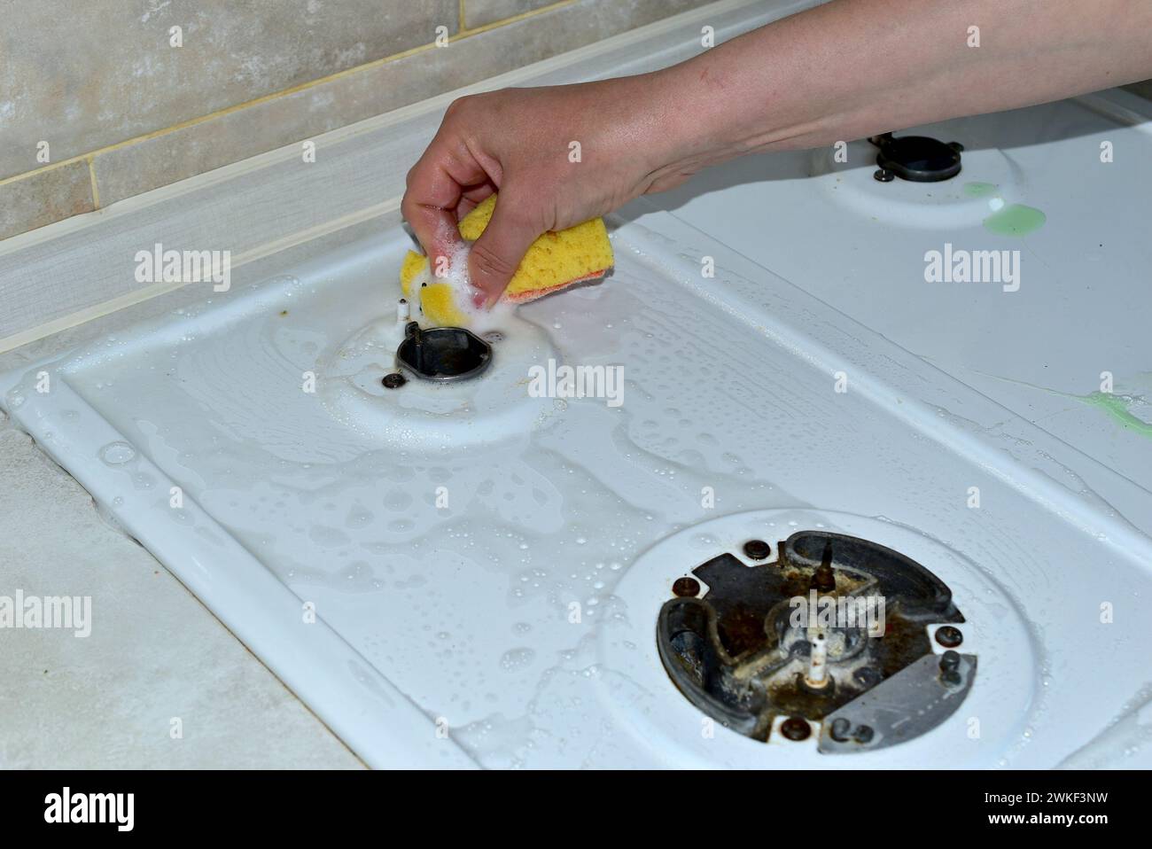 La femme lave la surface supérieure de la cuisinière à gaz autour du petit brûleur avec une éponge et des détergents. Banque D'Images