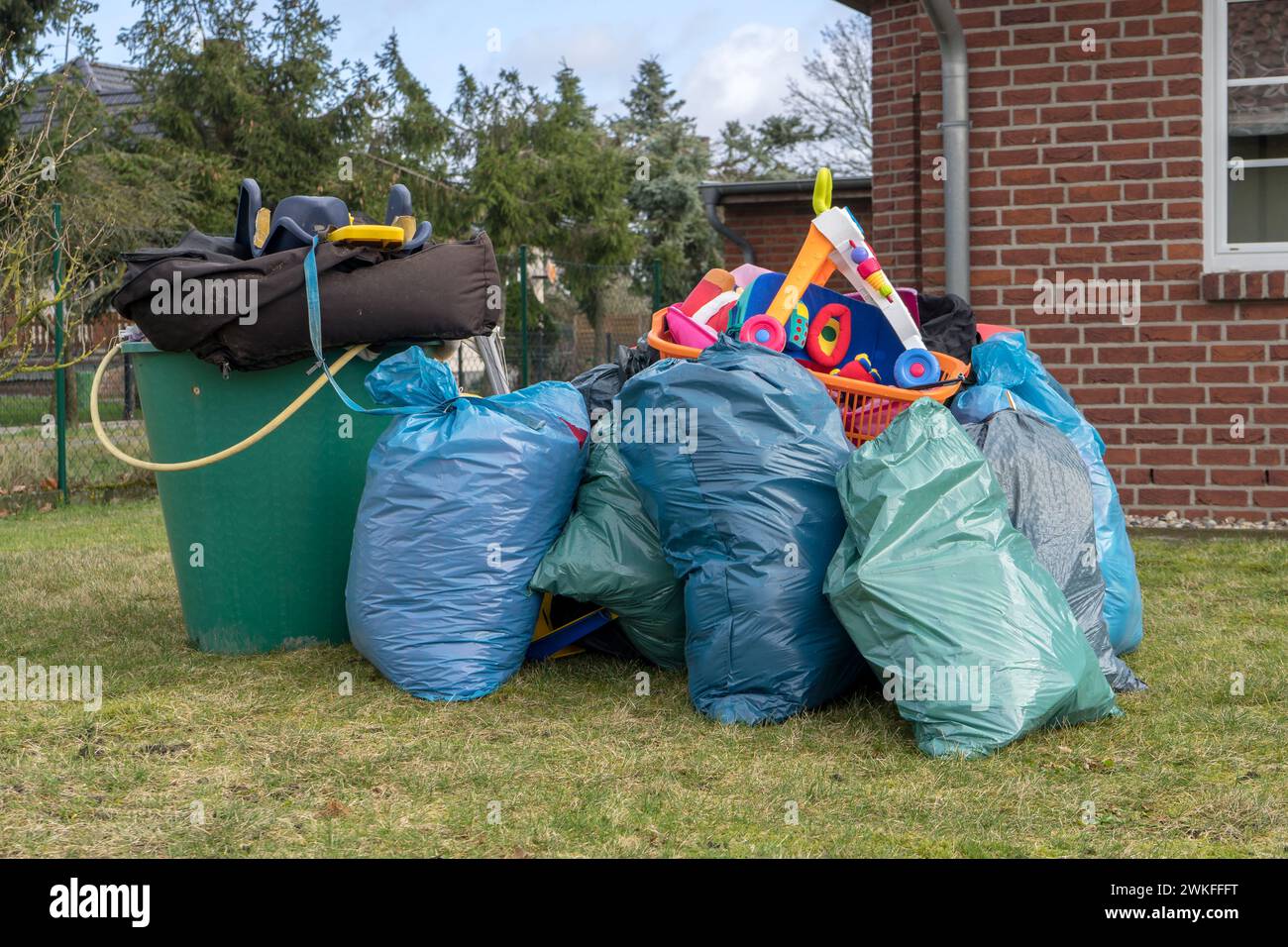 Pile de déchets encombrants devant une maison avec des sacs à ordures, des barils de pluie et des jouets Banque D'Images