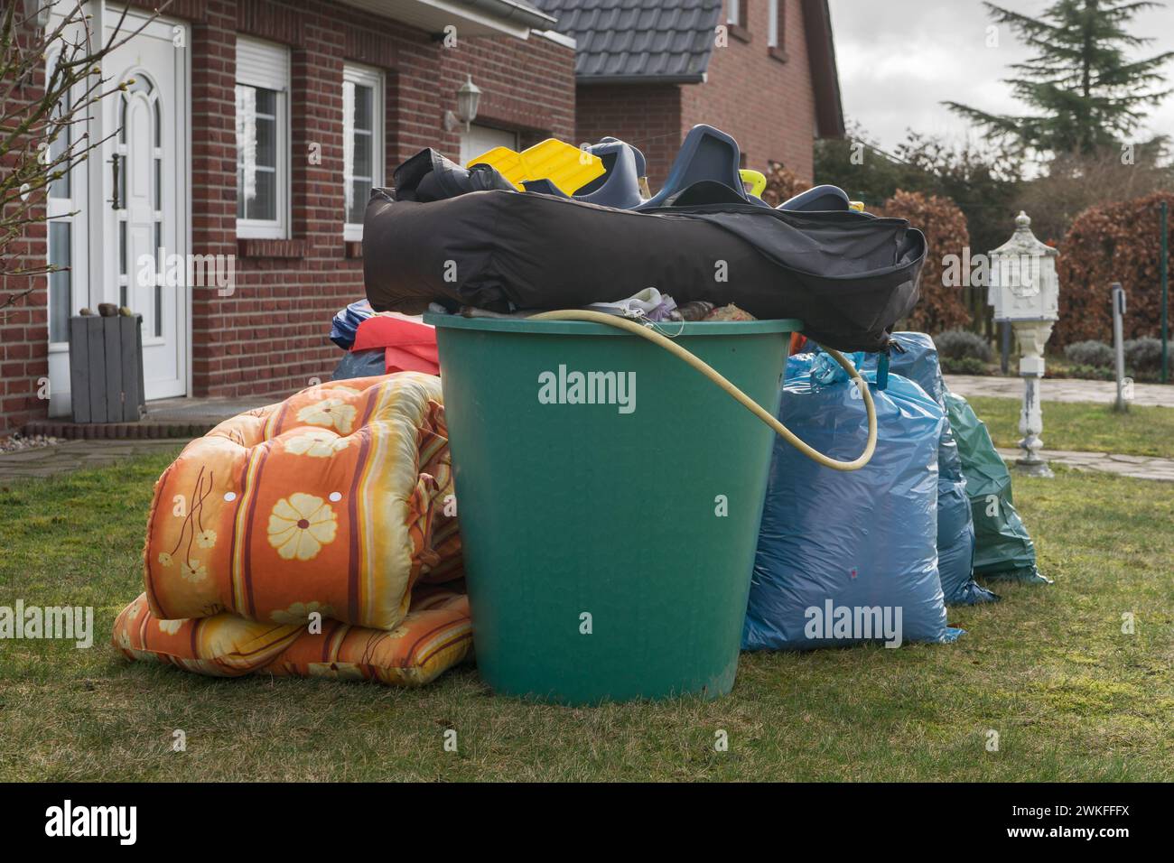 Pile de déchets encombrants devant une maison avec des sacs à ordures et des barils de pluie Banque D'Images