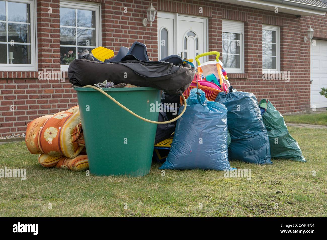 Pile de déchets encombrants devant une maison avec des sacs à ordures et des barils de pluie Banque D'Images
